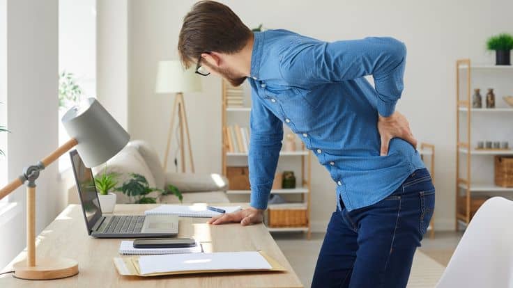 a man holding his back while leaning on a desk