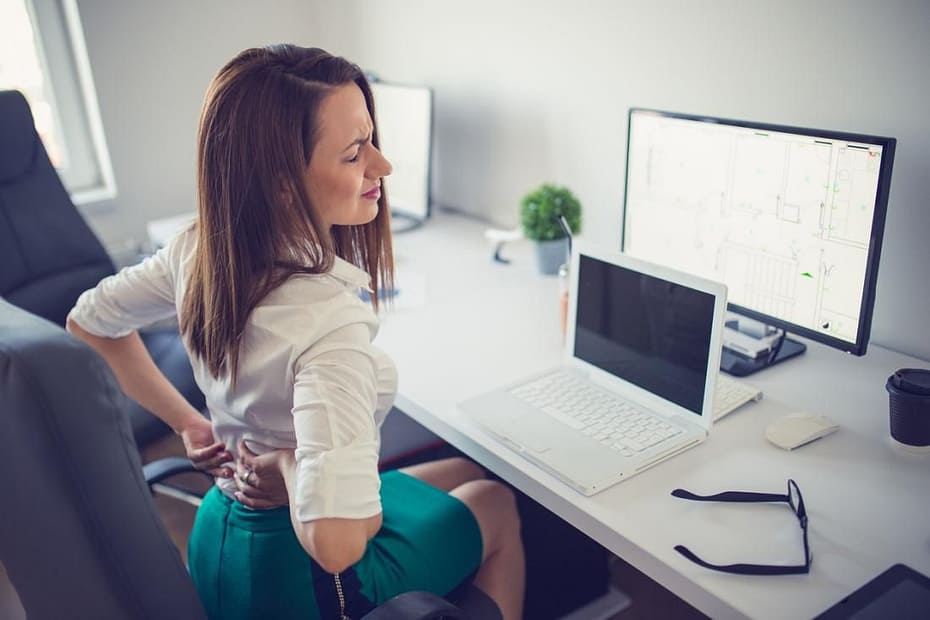 a woman holding her back while sitting at a desk with a computer